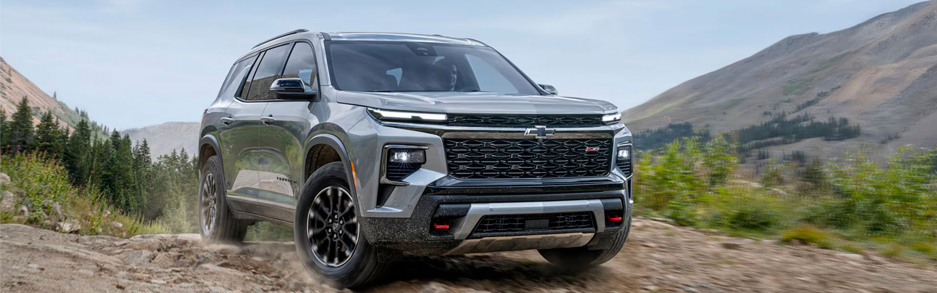 Silver 2026 Chevrolet Traverse tackling rugged terrain, featuring a bold front-end design, high ground clearance, and confident off-road presence.